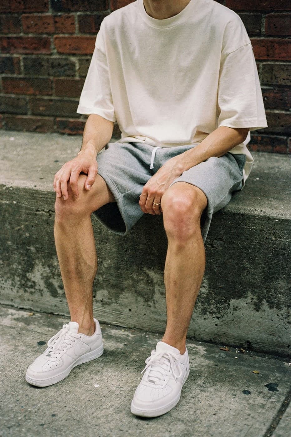 A white boxy tee, grey fleece shorts and white sneakers on a concrete stoop